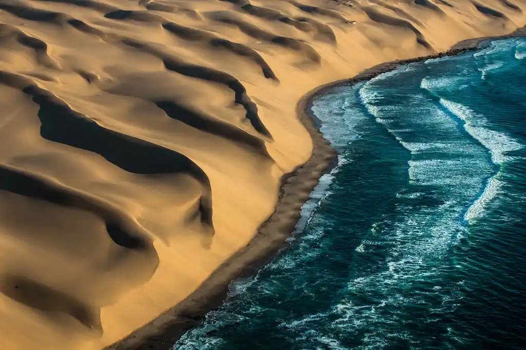Namib Desert coastline where towering sand dunes meet the Atlantic Ocean — a dramatic, remote wilderness ideal for explorers seeking offbeat adventure travel, raw landscapes, and unique desert-meets-sea experiences.